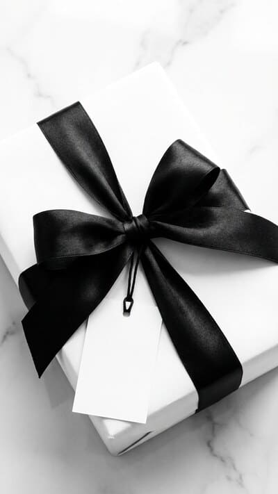 Elegantes Geschenk in weißem Papier verpackt mit schwarzem Satinband und schlichtem Anhänger für Scandi-Vibes.