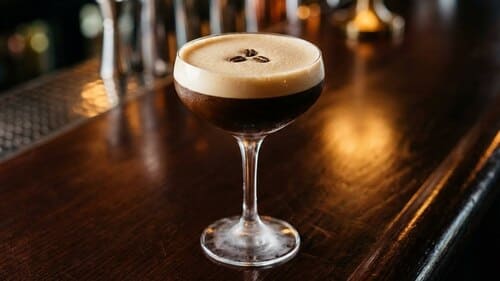 Nahaufnahme eines cremigen Espresso-Drinks in einem eleganten Glas, garniert mit drei Kaffeebohnen auf dem Schaum.