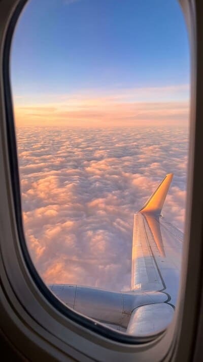 Atemberaubender Blick aus dem Flugzeugfenster auf einen Sonnenaufgang über weißen Wolken. Die Flugzeugtragfläche liegt ruhig in der Sonne. Symbol für die Freiheit des Reisens.