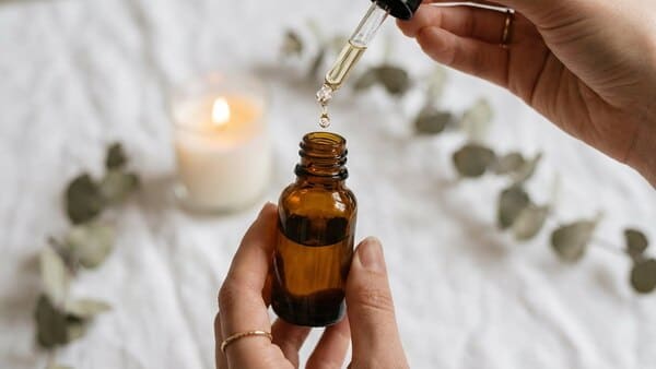 Hände halten ein kleines braunes Fläschchen ätherisches Öl über ein ruhiges Spa-Setting.