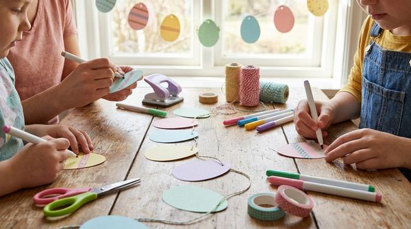 Bunte Papier-Eier werden bemalt und als Girlande auf eine Schnur gefädelt