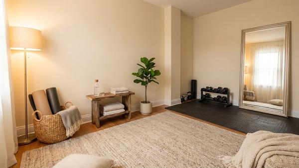 Gemütlicher Homegym-Raum mit Yogamatten-Ecke, warmem Lampenlicht, Korb für Zubehör und ruhigen Farben