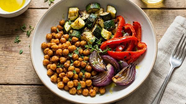 Bowl mit knusprigen Kichererbsen, geröstetem Gemüse und einem cremigen Dip als Topping.