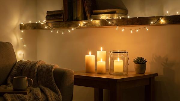 Gemütliche Ecke mit warm leuchtender Lichterkette, Kerzen und Windlichtglas am Abend.