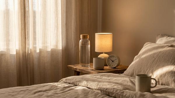 Nachttisch am Morgen mit Trinkflasche, Wecker und warmem Licht für eine einfache Morgenroutine