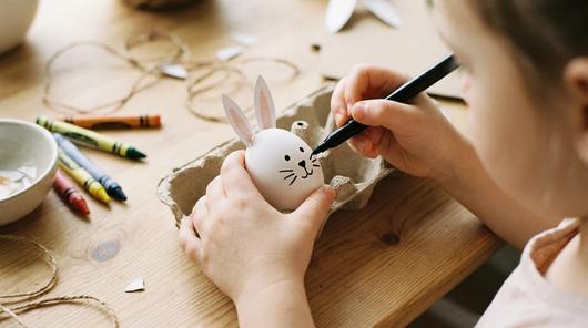 Osterei mit Hasengesicht und Papierohren, Kind malt Schnurrhaare auf