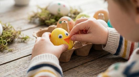 Gelbes Osterei als Küken mit Wackelaugen und kleinem Schnabel im Eierkarton