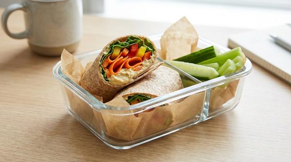 Aufgeschnittener Wrap mit Hummus, Karotte, Paprika und Salat in einer Lunchbox.
