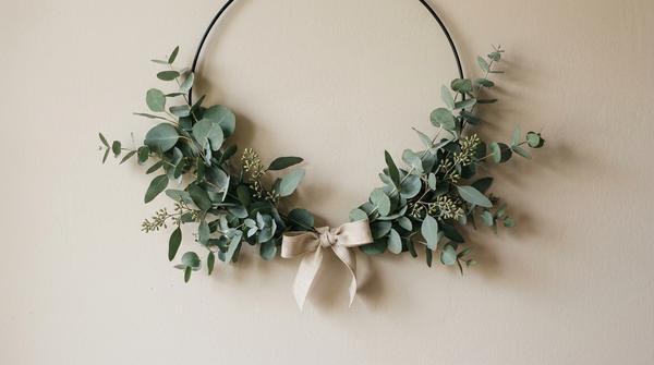 Du siehst einen minimalistischen Eukalyptus-Kranz auf einem dünnen Metallring mit einer kleinen Leinen-Schleife.