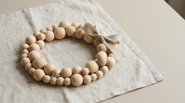 Du siehst einen modernen Kranz aus Holzperlen auf hellem Leinen mit einem kleinen Oster-Akzent.