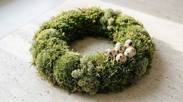 Du siehst einen runden Mooskranz auf hellem Untergrund mit einem kleinen Akzent aus Wachteleiern.