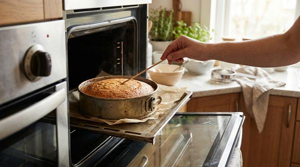 Stäbchenprobe an einem Kuchen in einer Backform im Ofen, das Blech ist mit Backpapier ausgelegt und die Ofentemperatur ist am Drehregler eingestellt.