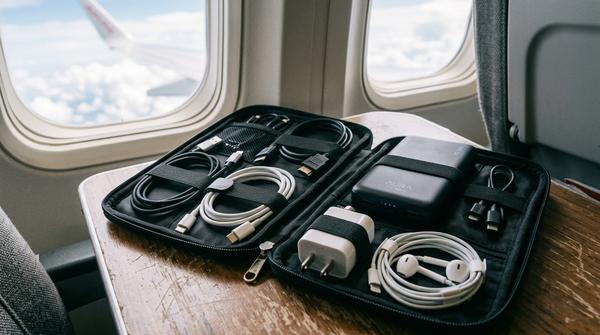 Eine offene Kabel-Organizer-Tasche auf einem Flugzeugtisch, ordentlich gefüllt mit Ladekabeln, Adaptern und einer Powerbank.