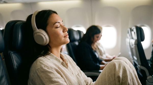 Ein Passagier trägt Noise-Cancelling-Kopfhörer im Flugzeug und schließt entspannt die Augen.