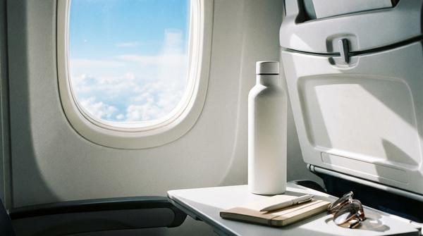Eine moderne, wiederverwendbare Trinkflasche steht auf dem ausklappbaren Tisch im Flugzeug.