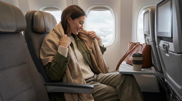 Eine Person im Flugzeug hüllt sich in einen großen, weichen Schal im praktischen Zwiebellook.