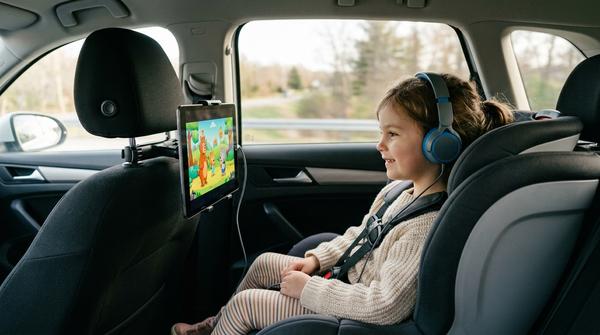 Kind schaut Film auf Tablet in Halterung auf Auto-Rückbank