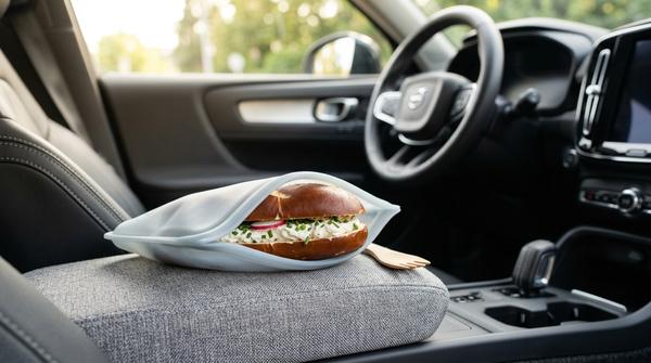 Ein halbiertes Laugenbrötchen mit Frischkäse ohne grobes Salz, sauber verpackt in einem wiederverwendbaren Silikonbeutel im Auto.