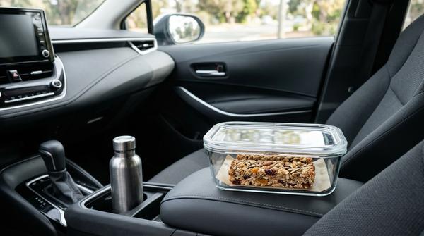 Zwei softe, selbstgebackene Hafer-Müsliriegel liegen ordentlich nebeneinander in einer Frischhaltedose aus Glas im Auto.