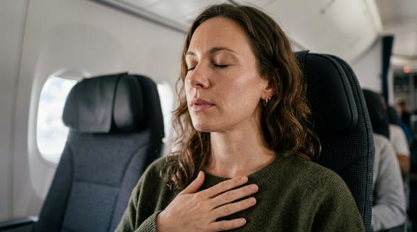 Frau sitzt im Flugzeug mit geschlossenen Augen und konzentriert sich auf ruhiges Atmen